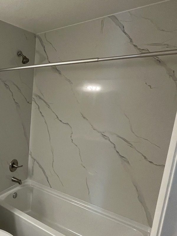 Hall bath tub with a marble-look surround and brushed nickel fixtures