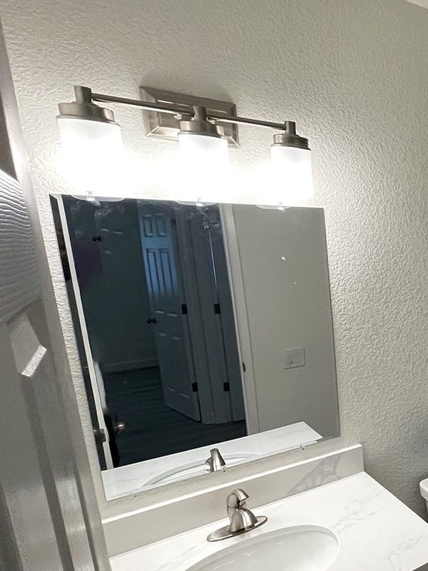 Hall bath vanity with a white top, a brushed nickel faucet and a three-light fixture over the mirror