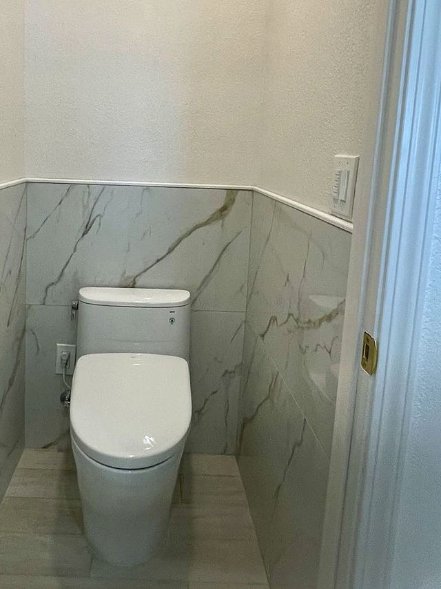 Separate toilet room with marble-look tile wainscot and a herringbone tile floor beyond